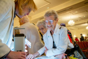 A group of elderly women at an information desk, with one woman smiling and interacting with a staff member.