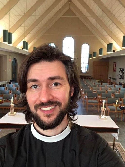 A headshot of Reverend Andrew Goldhor, standing at the front of a church sanctuary