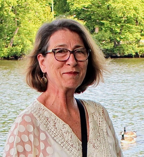 Paula Halpin, wearing glasses, stands beside the Charles River in Watertown